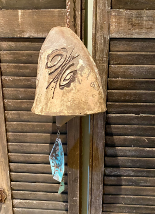 A decorative ceramic bell with etched eye designs, hanging from a chain against a wooden background.